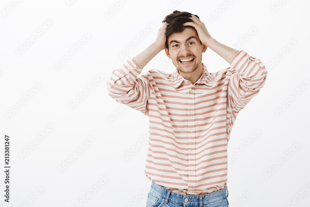 Positive friendly guy never gets upset easily. Portrait of handsome happy man with beard and moustache, holding hands on head and smiling while remembering something he forgot over gray wall Positive friendly guy never gets upset easily. Portrait of handsome happy man with beard and moustache, holding hands on head and smiling while remembering something he forgot over gray wall