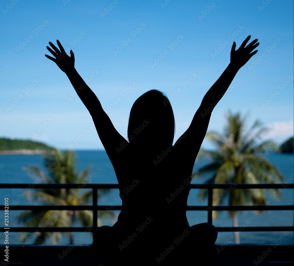 Silhouette of happy woman raising arms looking view on the beach with sea and blu sky background Silhouette of happy woman raising arms looking view on the beach with sea and blu sky background