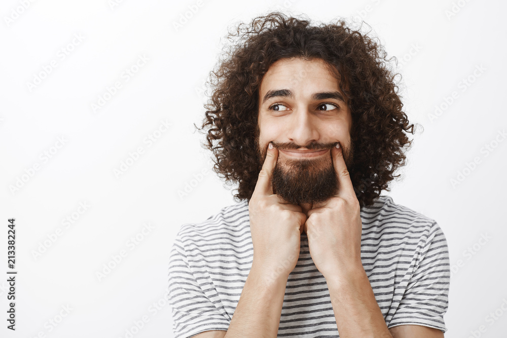 Portrait of stressed upset attractive bearded man with curly hair, pulling smile with index finger and looking left with sad expressions, being bored, having nothing to do after friends went home Portrait of stressed upset attractive bearded man with curly hair, pulling smile with index finger and looking left with sad expressions, being bored, having nothing to do after friends went home