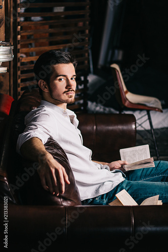 Handsome businessman is reading a book, holding eyeglasses and smiling while sitting on couch at home © Алекс Кис