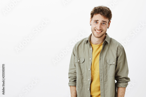 Waist-up shot of arrogant handsome and self-assured curly-haired male with bristle, laughing and looking wish disdain at camera, standing over gray background careless and indifferent