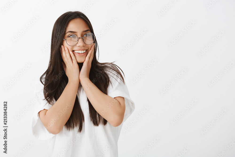 So sweet receiving compliments. Portrait of positive happy good-looking female coworker in glasses and white t-shirt, looking right and holding palms on cheeks while smiling from satisfaction So sweet receiving compliments. Portrait of positive happy good-looking female coworker in glasses and white t-shirt, looking right and holding palms on cheeks while smiling from satisfaction