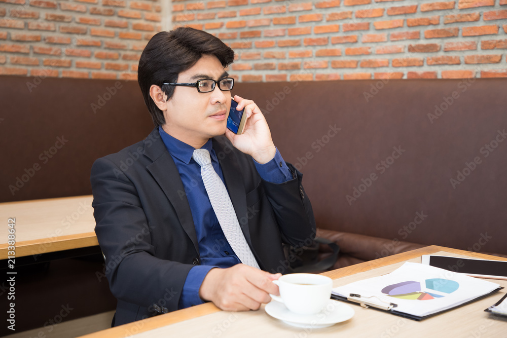 Asian businessman drinking coffee in office using phone Asian businessman drinking coffee in office using phone