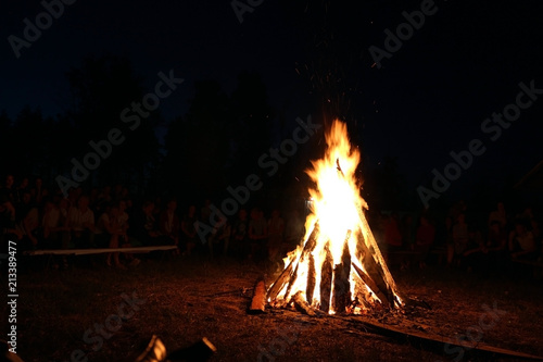 Blurred People sit at night around a bright bonfire