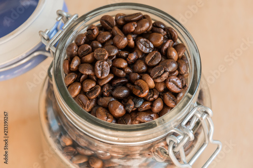 Coffee beans in a glass jar on wooden background closeup. Roasted aromatic coffee top view.