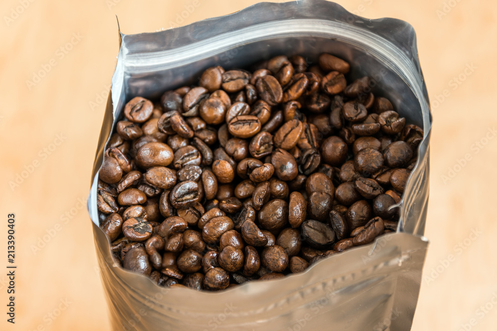 Fototapeta premium Coffee beans in a plastic foil package on wooden background. Roasted aromatic coffee top view.