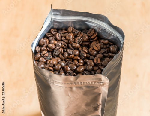 Coffee beans in a plastic foil package on wooden background. Roasted aromatic coffee top view.