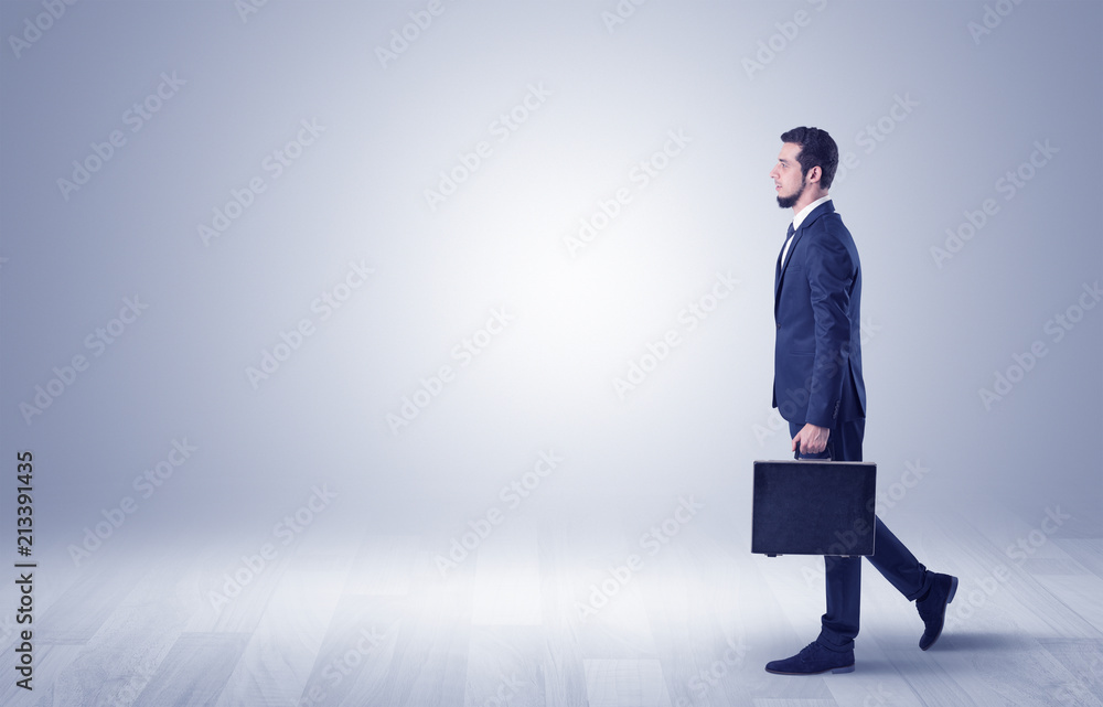 Successful businessman walking in front of an empty wall with briefcase on his hand
