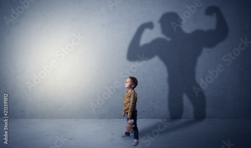 Little waggish boy in an empty room with musclemen shadow behind 