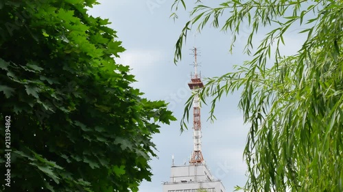 High antenna or feeler on the building at blue sky with white clouds background. Communication station, telecommunication or broadcasting equipment