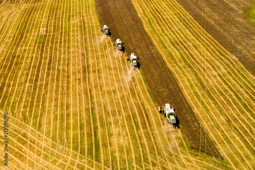Aerial shot of four combine harvester harvesting wheat field on a sunny summer day