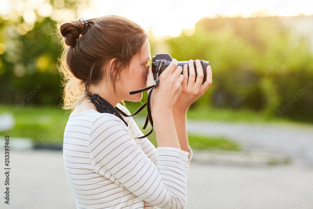 young girl taking pictures on camera in a summer Park at sunset