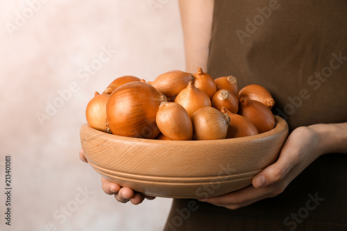 Woman holding bowl with ripe onions on grey background