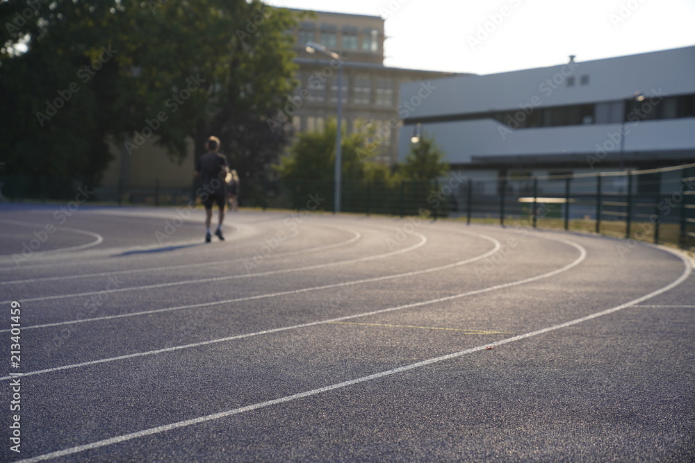 Blue outdoor stadium running track with white dividing lines and a blurred person running on the background