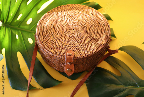 Round shaped Ata rattan boho bag with a leather strap laying on a Monstera leaf and yellow, sunny background photo