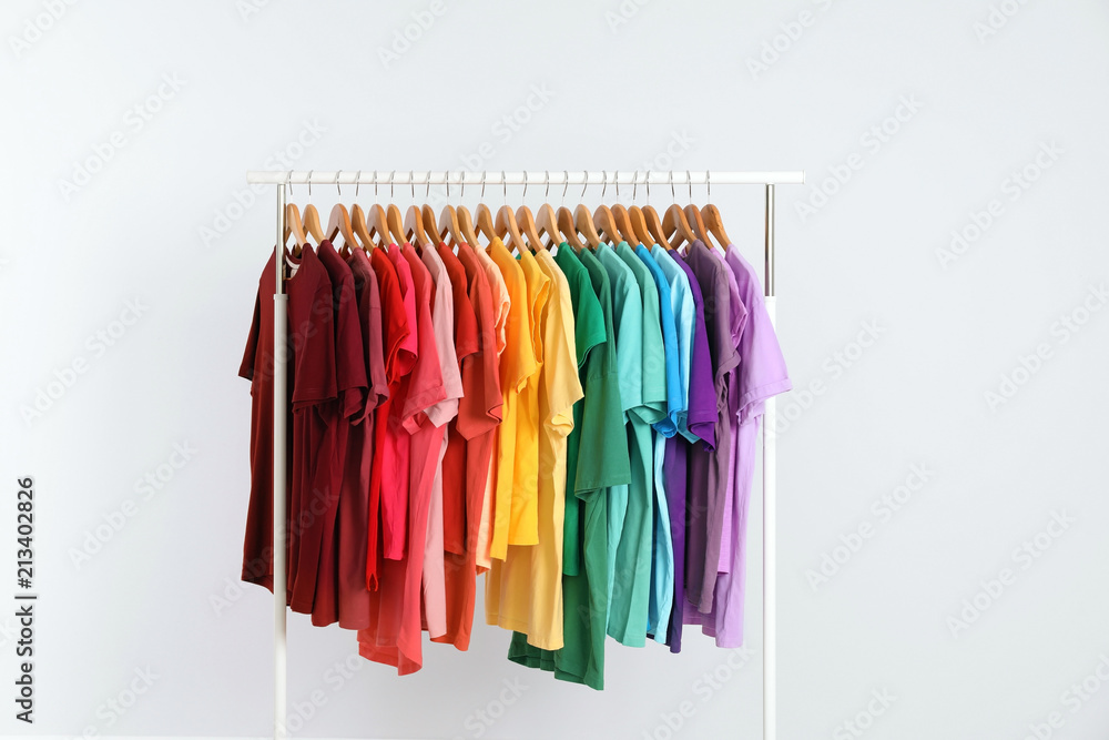 Rack with rainbow clothes on light background