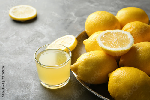 Plate with ripe lemons and glass of fresh juice on table