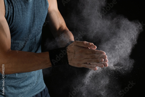 Young man applying chalk powder on hands against dark background