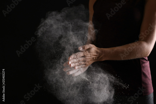 Young woman applying chalk powder on hands against dark background © New Africa