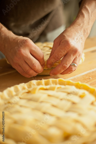 A man's hands preparing the crimped pastry crusts of two unbaked apple pies. Vertical image with shallow depth of field.