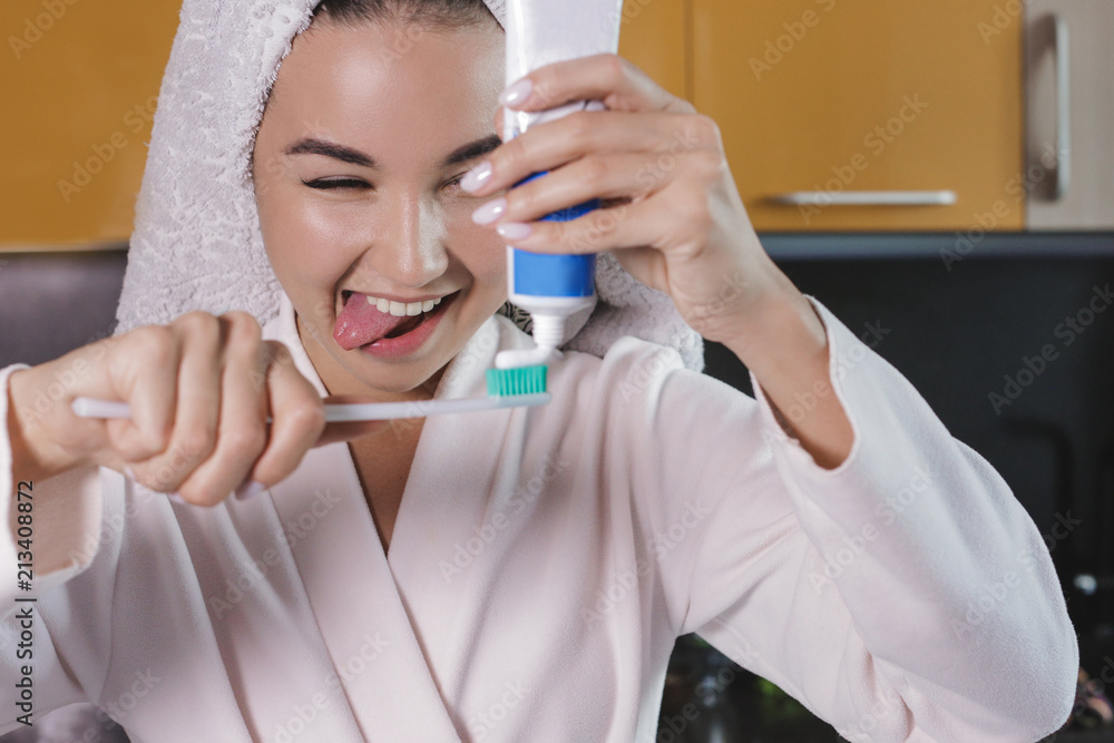 Naklejka premium naughty young beautiful girl with a towel on her head brushing her teeth. squeezing toothpaste