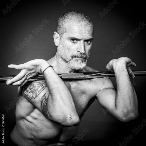 A man 50 Y is holding an outrigger raising the weights. Black background. photo