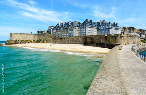 Fototapeta The walled city of Saint-Malo in Brittany, France, with granite residential buildings sticking out above the rampart and people sunbathing on the Mole beach at the foot of the high wall