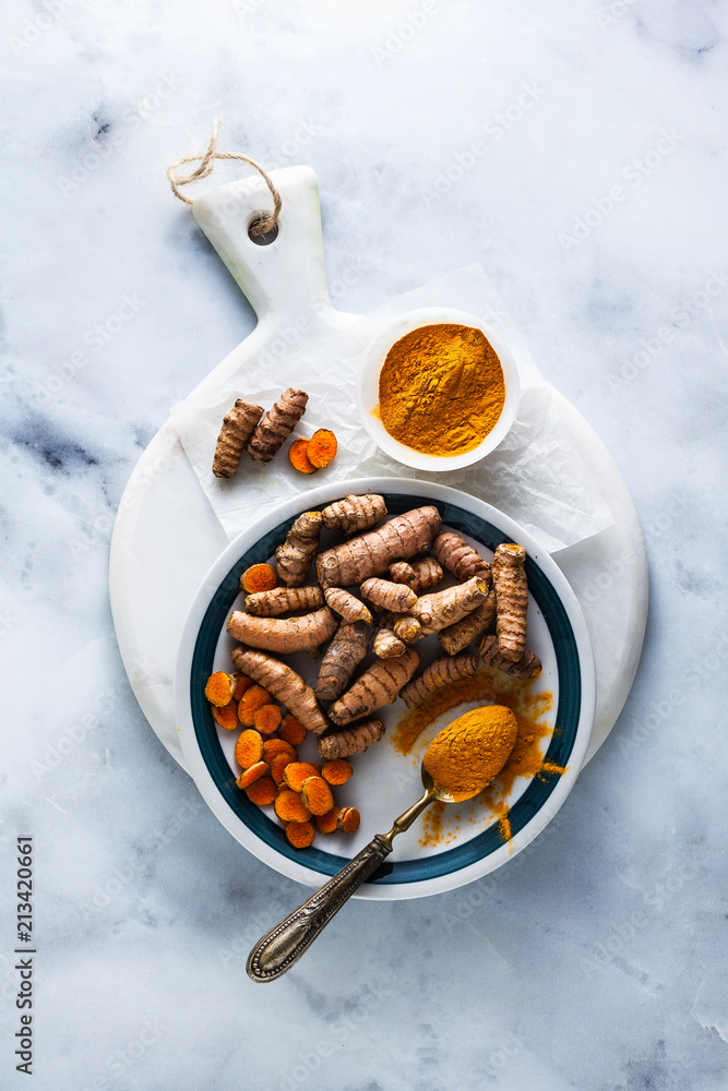 roots of turmeric and powder from it on a white marble board and table. healthy natural supplements, spices for cooking roots of turmeric and powder from it on a white marble board and table. healthy natural supplements, spices for cooking
