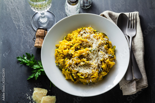 Italian dish yellow Risotto milanese with saffron, zucchini and Parmesan cheese on a black slate table with white wine in a glass. north Italy kitchen