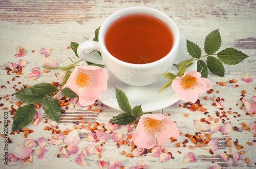 Vintage photo, Cup of tea with wild rose flower on old rustic board