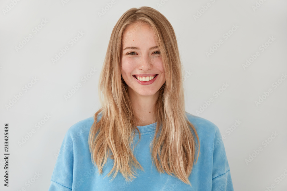 Pretty smiling blonde female with appealing tender look, has joyful expression, clean skin, being in high spirit after recieving compliment from handsome guy, stands against white background. Pretty smiling blonde female with appealing tender look, has joyful expression, clean skin, being in high spirit after recieving compliment from handsome guy, stands against white background.