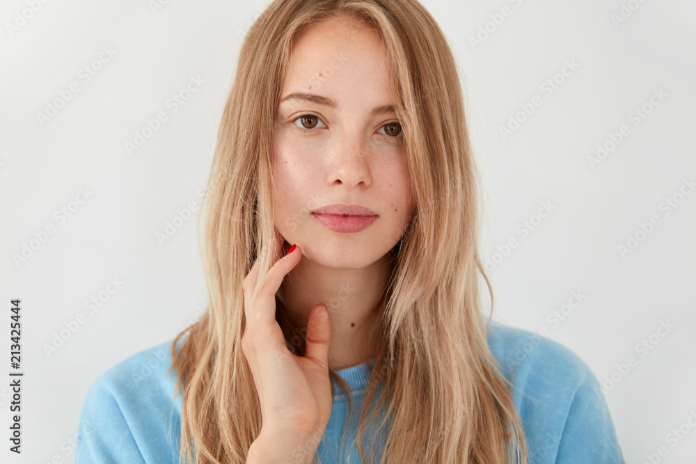 Close up shot of attractive blonde young female student with serious facial expression, thinks about passing exam, looks directly at camera, spends free time at home, isolated over white background Close up shot of attractive blonde young female student with serious facial expression, thinks about passing exam, looks directly at camera, spends free time at home, isolated over white background