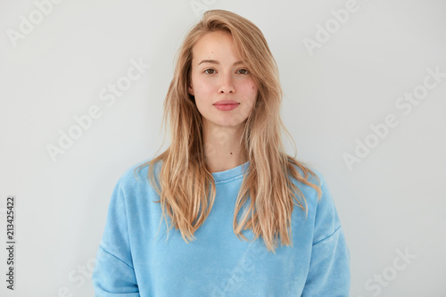 Canvastavla Adorable blonde female with serious expression, dressed in blue sweater, has healthy clean skin, isolated over white background