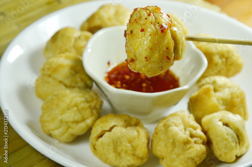  crispy fried fish ball stabbing in wooden stick dipping spicy and sweet sauce cup on plate