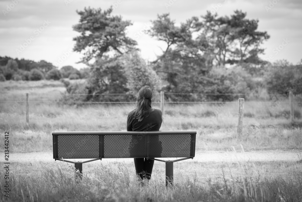 Eine junge Frau sitzt einsam auf einer Bank. Schwarz-weiss Foto Stock-Foto  | Adobe Stock