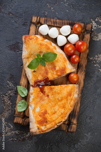 Tableau sur toile Sliced italian pizza calzone on a rustic wooden serving tray, flatlay on a brown
