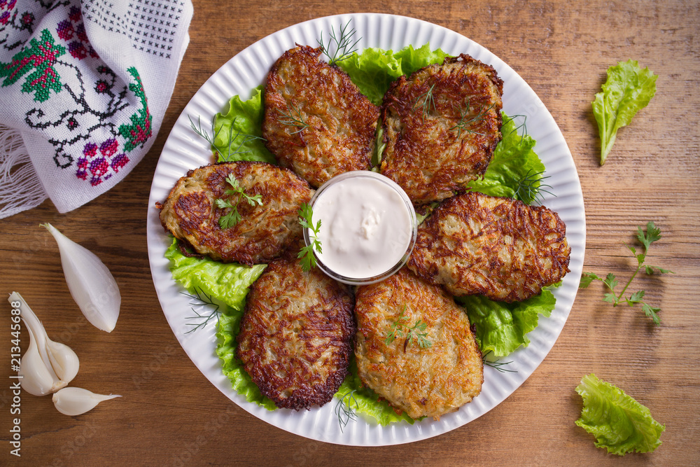 Potato fritters, latkes, draniki, hash browns - popular dish in many countries. Vegetable pancakes on white plate, wooden table. overhead, horizontal Potato fritters, latkes, draniki, hash browns - popular dish in many countries. Vegetable pancakes on white plate, wooden table. overhead, horizontal