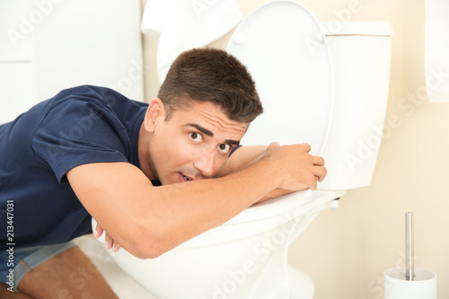 Young man vomiting in toilet bowl at home photo