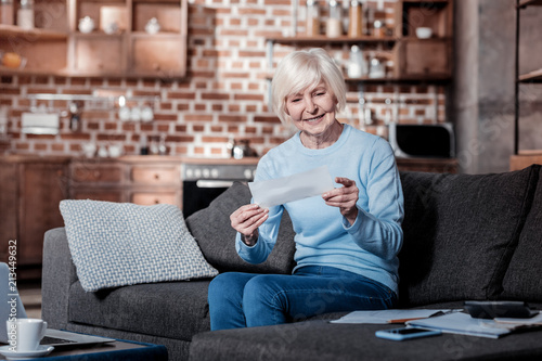 Checking bill. Joyful pensioner keeping smile on her face while checking documents