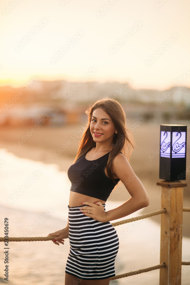 Attractive girl walking on pier near the sea in sunset time Attractive girl walking on pier near the sea in sunset time