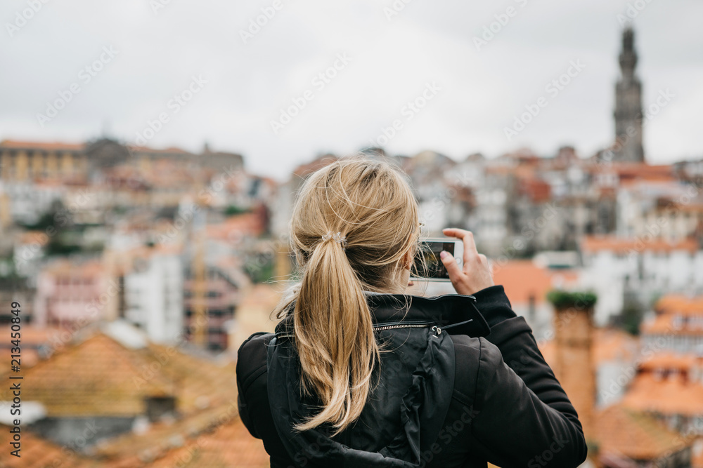 A tourist girl at the observation deck takes pictures of a beautiful view of the city in Porto in Portugal on a mobile phone