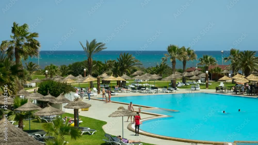 Beautiful tropical beach front hotel resort with swimming pool, sun-loungers and palm trees during a warm sunny day, paradise destination for vacations. Time Lapse. Timelapse. Beautiful tropical beach front hotel resort with swimming pool, sun-loungers and palm trees during a warm sunny day, paradise destination for vacations. Time Lapse. Timelapse.