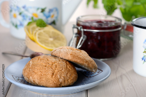 The cookie on the paper mat is next to the slices of lemon and jam in jar on the table