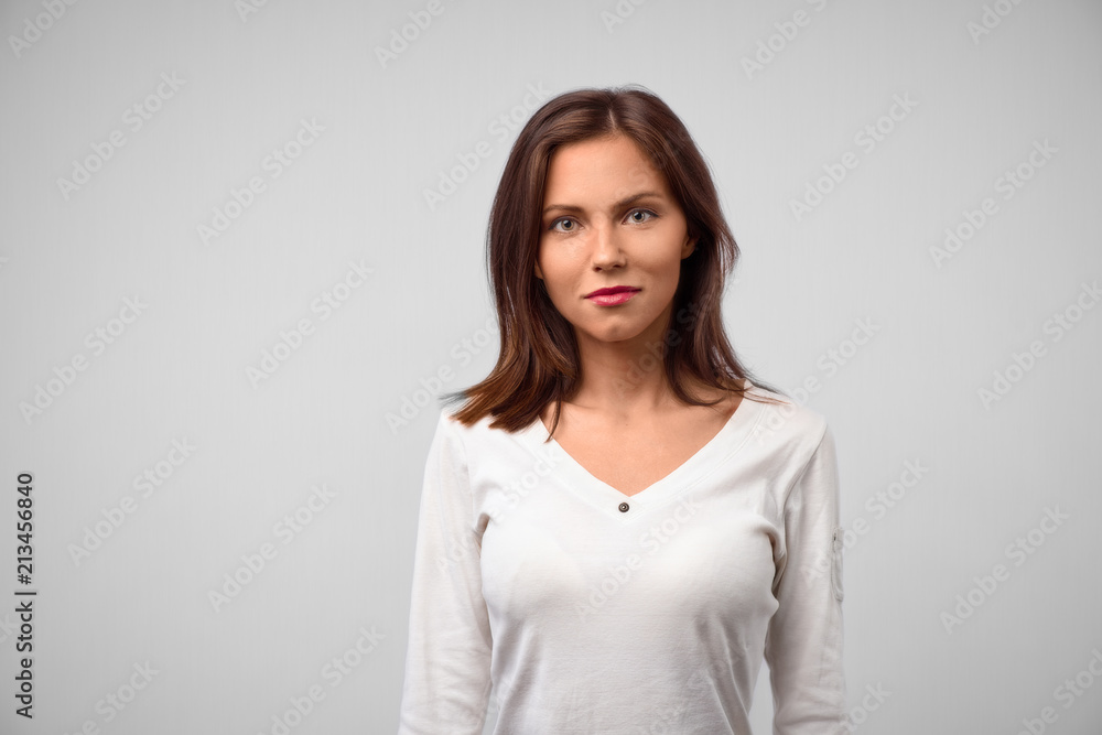 Attractive teenager with confident look, has long straight hair, dressed casually, smiles gently, looks directly at camera, reads necessary information in front, stands against white concrete wall Attractive teenager with confident look, has long straight hair, dressed casually, smiles gently, looks directly at camera, reads necessary information in front, stands against white concrete wall