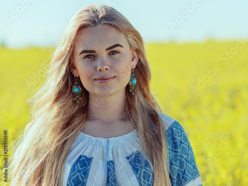 Portrait of a beautiful young paesant woman in a blooming flower field. Romanian girl with traditional shirt smilling and enjoying a sunny day in a countryside photo