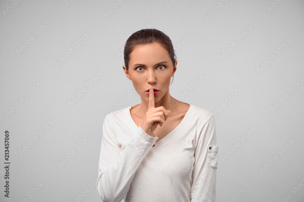 Shh, keep this secret from anyone. Portrait of feminine stylish woman, showing shush gesture with index finger over mouth, folding lips, asking keep quiet or silence Shh, keep this secret from anyone. Portrait of feminine stylish woman, showing shush gesture with index finger over mouth, folding lips, asking keep quiet or silence
