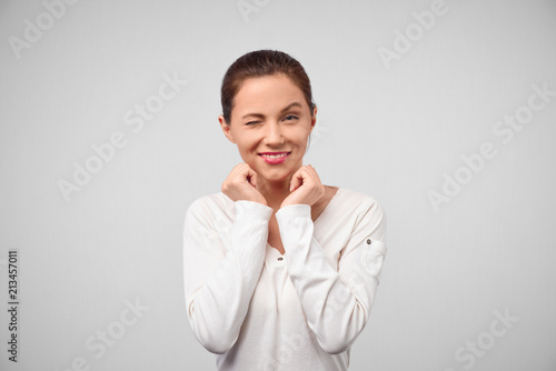 Cheerful young beautiful girl smiling winking looking at camera over white background. Close-up studio shot of positive young European woman smiling happily, blinking at camera in playful manner