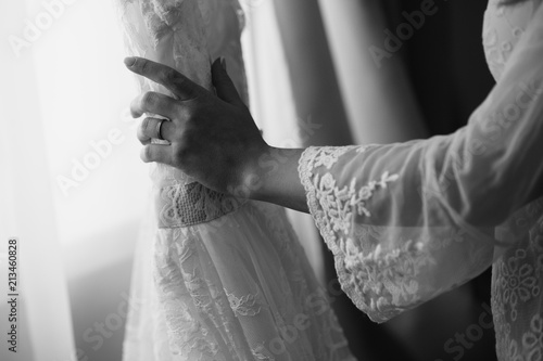 Black and white photo of bride hand with engagement or wedding ring holding a luxury wedding dress with lace. Preparation for bridal ceremony. At home © Wedding photography