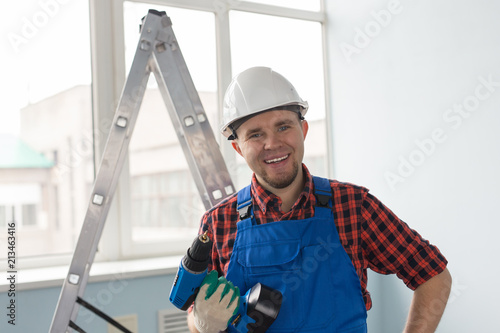 Closeup portrait of happy white male builder with drill wearing white helmet.
