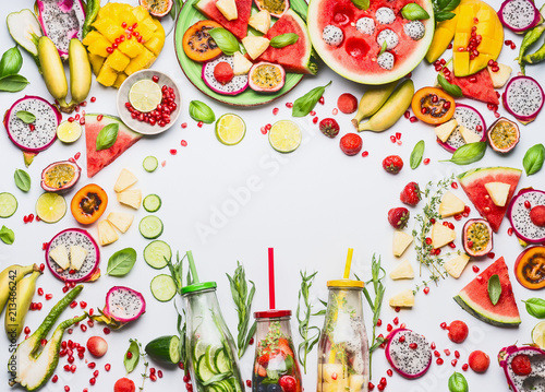 Summer clean and healthy lifestyle and fitness background with various colorful sliced fruits, berries, vegetables ,herbs, infused water in bottles on white background, top view, frame